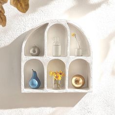 a white shelf with vases and other items on top of it next to a wall