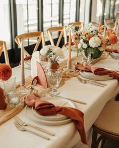 the table is set with white and orange plates, silverware, napkins, and flowers