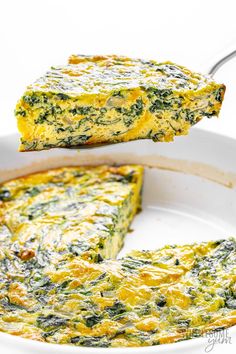 an omelet with spinach and cheese is being lifted from the pan by a fork