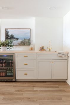 a kitchen with white cabinets and wood flooring has a wine cooler in the middle