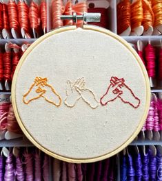 two hands holding each other in front of some thread spools and embroidery hoop