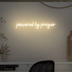 a neon sign that reads powered by prayer on the wall above a chair and vase