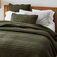 a bed with green bedspread and pillows on top of it, next to a lamp