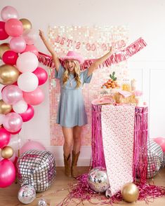 a woman standing in front of a table with pink and gold balloons on the wall