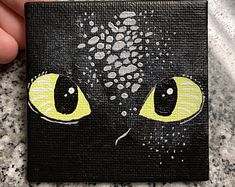 a painting of a black cat's face with yellow eyes on a black background