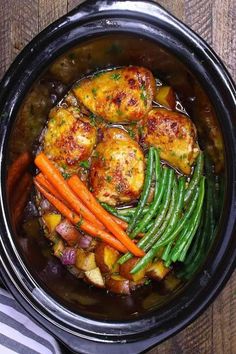 a crock pot filled with chicken, potatoes and carrots on top of a wooden table