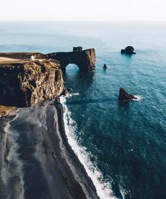 an aerial view of the ocean with cliffs in the foreground and black sand beach below