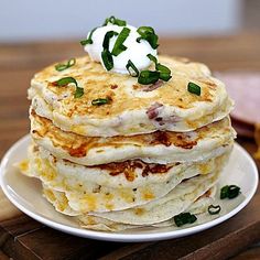 a stack of pancakes on a plate with sour cream and green onion garnish