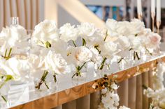 white flowers in vases are lined up on a long table with gold trimming