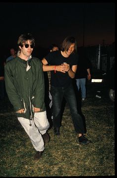 two young men standing next to each other on top of a grass covered field at night