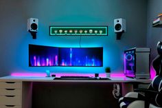 a computer desk with two monitors and speakers on top of it, lit up by neon lights