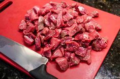 chopped meat on a red cutting board with a knife next to it, ready to be cooked