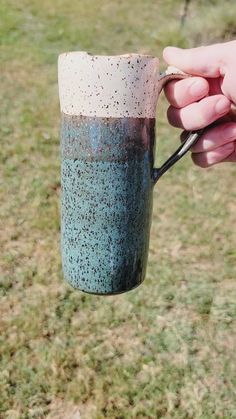 a person holding a coffee cup in their hand with grass and trees in the background