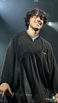 a man standing in front of a microphone and wearing a black shirt with an embellishment on his face