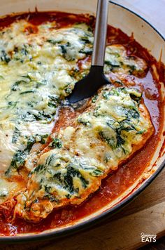 a pan filled with lasagna sauce and spinach covered in cheese on top