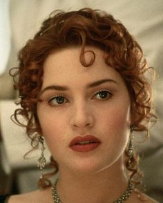 a close up of a woman with curly hair and blue eyes wearing pearls on her head