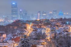 the city skyline is lit up at night with snow on the ground and buildings in the foreground