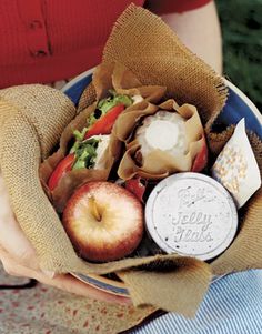 a person holding a bag full of assorted food items in their hands, including an apple and cheeseburger