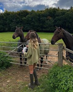 a woman standing in front of horses behind a fence