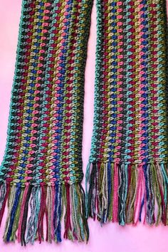 a multicolored crocheted scarf with fringes on top of pink background