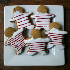 gingerbreads decorated with white and red stripes are on a square plate, ready to be eaten