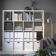 a white bookcase filled with lots of books next to a gray couch and potted plant