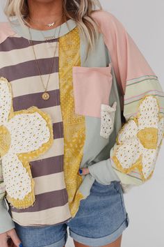 a woman wearing shorts and a sweater with crocheted flowers on the sleeves is standing in front of a white background