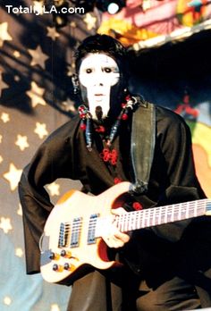 a man with white face paint playing an electric guitar in front of a stage backdrop