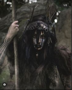 a man with black makeup and long hair holding a stick in front of his face