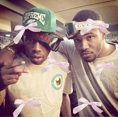 two men wearing hats with pink ribbons around their eyes and one man pointing at the camera