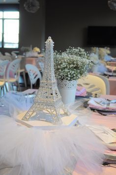 the table is set up for an event with white linens and flowers in front of the eiffel tower