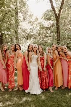 a group of women standing next to each other in front of trees and grass with one woman wearing an orange dress