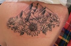 a woman's back with flowers and mountains on it