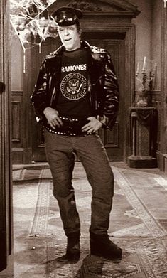 the man is wearing a leather jacket and standing in front of a door with his hands on his hips