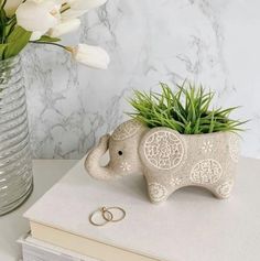 an elephant planter sitting on top of a table next to a vase with flowers