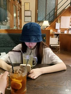 a woman sitting at a table with a drink in front of her and another person holding a cell phone