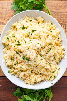 a white bowl filled with rice and parsley on top of a wooden table next to cilantro