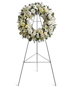 a wreath with white flowers and greenery on a black metal tripod easel