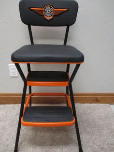 an orange and black harley davidson step stool next to a white wall with a harley davidson logo on it