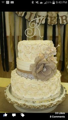 a three tiered wedding cake with white frosting and brown flowers on top is sitting on a table