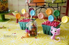 there are many buttons in the cupcakes on the table with pink and yellow candies