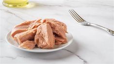 a white plate topped with sliced meat next to a fork and bottle of olive oil