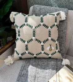 a pillow with a bee on it sitting on a chair next to a book and potted plant