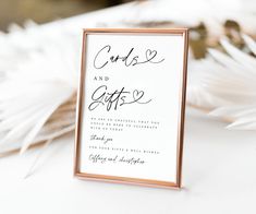 a white and gold wedding sign with black calligraphy on it, surrounded by feathers