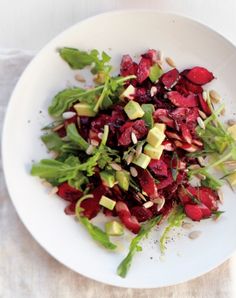 a white plate topped with beets and avocado on top of a table