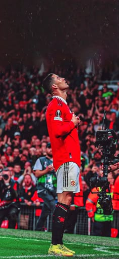 a man standing on top of a soccer field in front of a crowd holding a camera