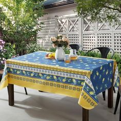 a blue table cloth with lemons and flowers on it in front of a white fence