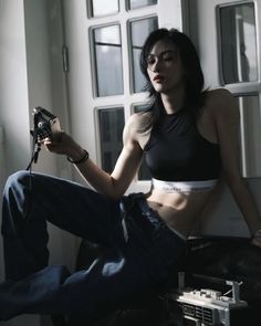 a woman sitting on top of a couch holding a camera next to a window with lots of windows behind her