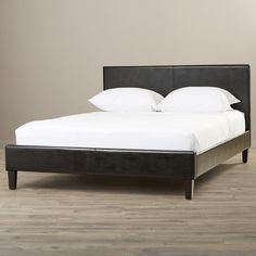 a bed with white sheets and pillows on top of wooden flooring next to a gray wall