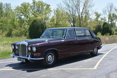 an old fashioned car parked in a parking lot next to some grass and trees on the other side of the road